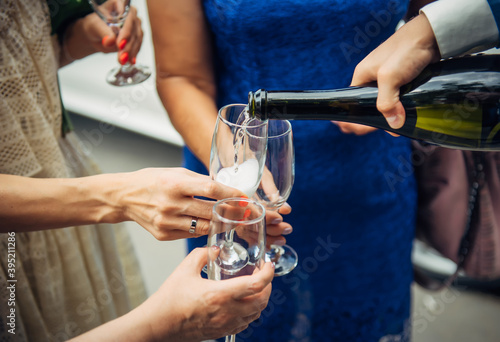 Man fills glasses of champagne for guests at festive dinner. Hand holding a bottle, close-up. Pouring drinks to friends and relatives at wedding banquet.