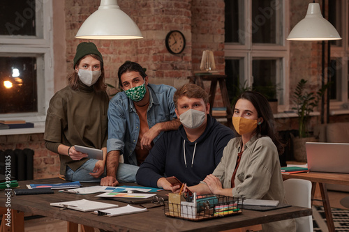 Portrait of group of designers in protective masks looking at camera during teamwork at office