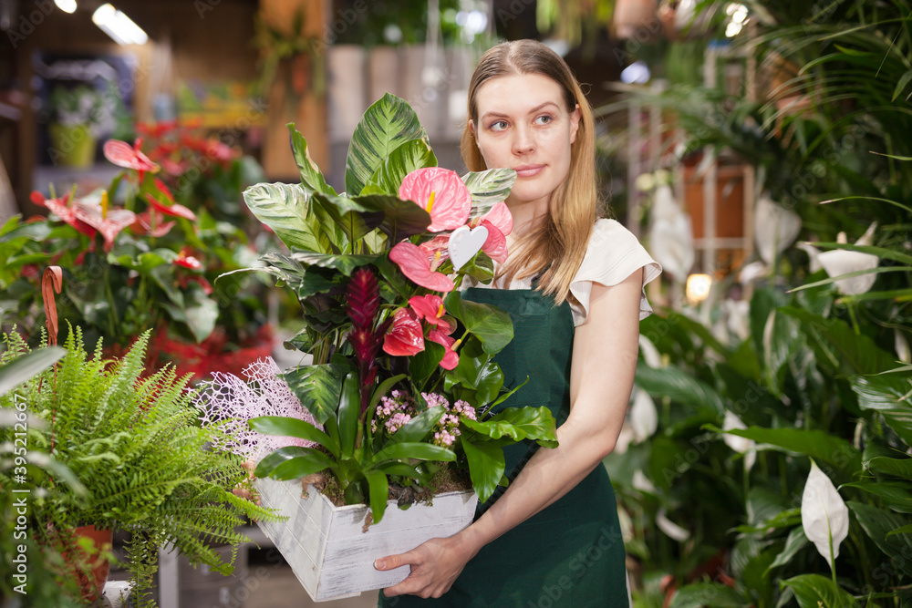 Cheerful woman florist holding pot with a flower in the gardening market. High quality photo