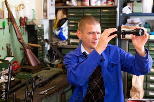 Portrait of professional craftsman engaged in adjusting optical sight in weapons workshop.