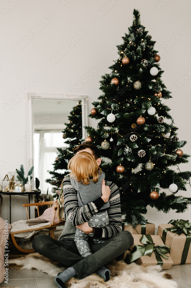 Merry Christmas and Happy Holidays. Cheerful father hugging cute baby daughter girl near Christmas tree. Dad and little child having fun and playing together at home. Merry Christmas and Happy Holidays. Cheerful father hugging cute baby daughter girl near Christmas tree. Dad and little child having fun and playing together at home.