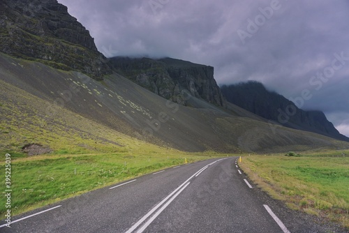 empty asphalt road bends at the foot of the mountains, heavy clouds hide the mountain tops, nature of Iceland