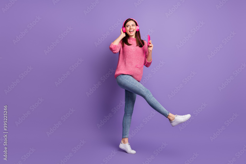 Full length body size photo of girl in earphones with mobile phone dancing kicking smiling isolated on vivid violet color background