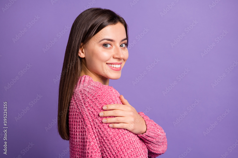 Side profile photo portrait of nice smiling female student embracing herself in pink sweater isolated on bright purple color background Side profile photo portrait of nice smiling female student embracing herself in pink sweater isolated on bright purple color background