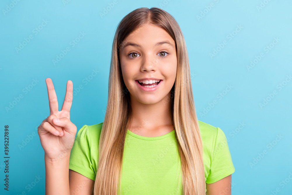 Portrait of young happy joyful smiling cheerful lovely pretty charming girl showing v-sign isolated on blue color background Portrait of young happy joyful smiling cheerful lovely pretty charming girl showing v-sign isolated on blue color background