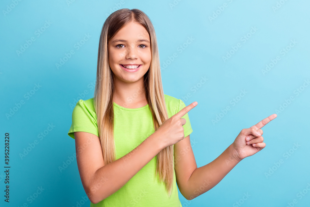 Portrait of young cheerful positive good mood girl smiling pointing finger in copyspace isolated on blue color background Portrait of young cheerful positive good mood girl smiling pointing finger in copyspace isolated on blue color background