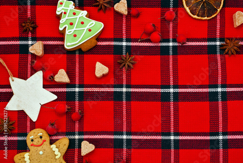 Christmas greeting card. Gingerbread man  sugar hearts  berries  fir shaped cookie and red berries on a red tartan background. Text space.