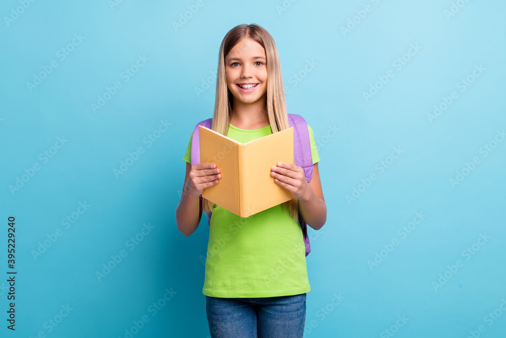 Photo of young happy positive good mood girl reding book wear purple rucksack isolated on blue color background Photo of young happy positive good mood girl reding book wear purple rucksack isolated on blue color background