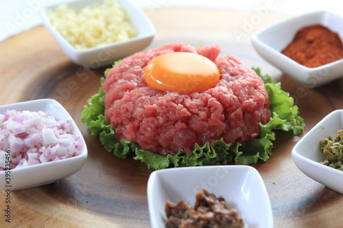 Traditional beef tartar served with a raw egg on top, onion and cucumber in white plate ready to be eaten
