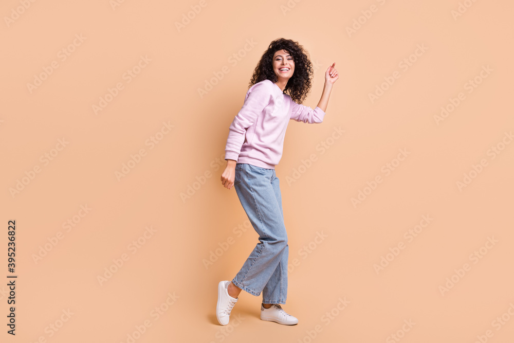 Full size profile photo of optimistic curly girl dancing wear sweater jeans sneakers isolated on peach color background Full size profile photo of optimistic curly girl dancing wear sweater jeans sneakers isolated on peach color background