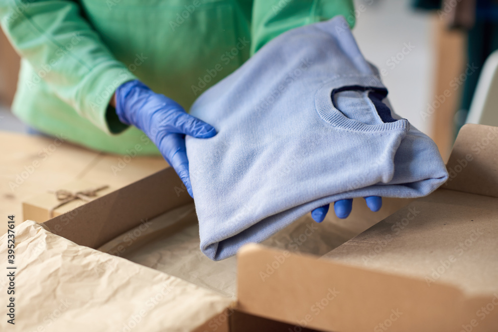 Close-up of woman in protective masks packing new clothes into the cardboard box and making parcel