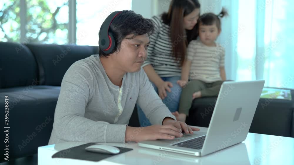 Young working father work from home while babysitting his playful daughter at home. Working father and daughter playing with mother on blur beside. Young working father work from home while babysitting his playful daughter at home. Working father and daughter playing with mother on blur beside.