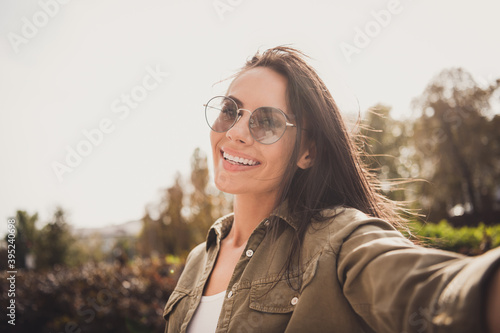 Photo of positive charming young lady take selfie beaming smile wear brown shirt spectacles park street outside