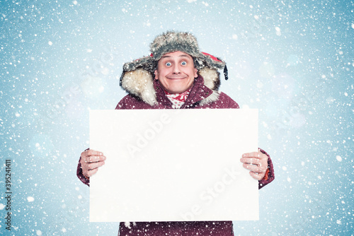 Happy smiling man in winter clothes holding a white banner in his hands. Snow falls.
