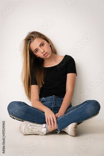 beautiful girl blonde teenager in jeans, black t-shirt and sneakers sits cross-legged © Alexander