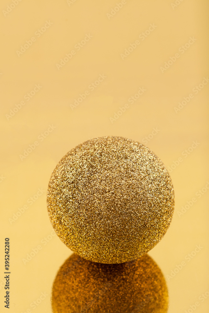 Sparkling golden christmas ball on golden mirror surface, close-up, selective focus. New year composition.
