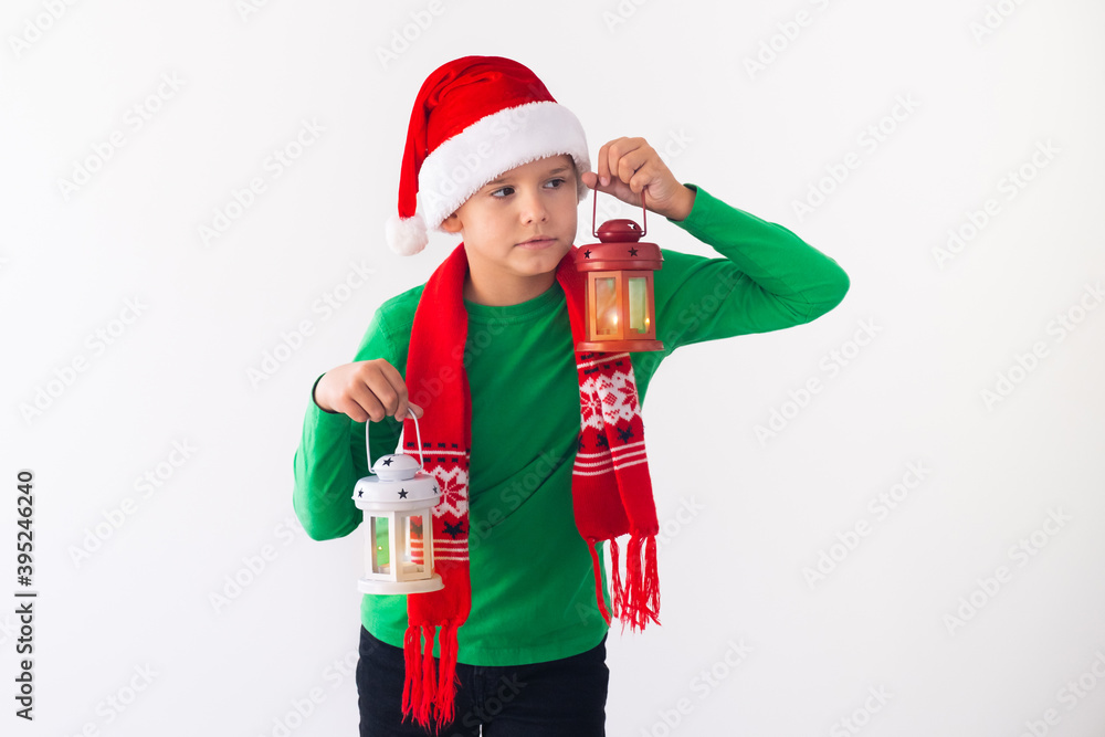 Portrait of boy wearing Santa hat and winter scarf. Scared child with lanterns in hands.
