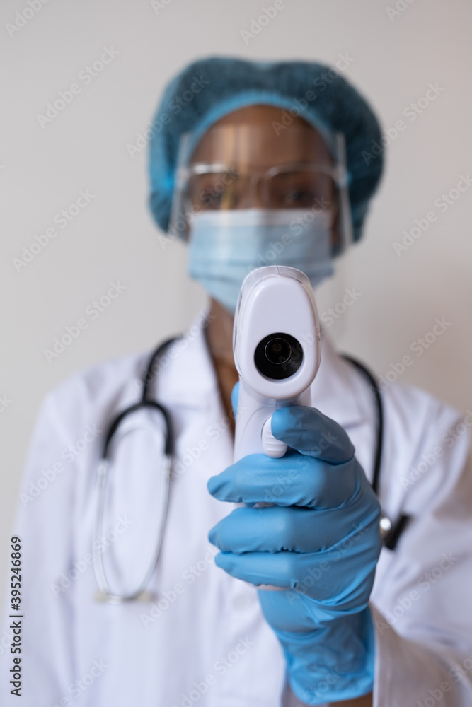 Medical worker with face shield in ppe with detail of thermometer taking temperature Medical worker with face shield in ppe with detail of thermometer taking temperature