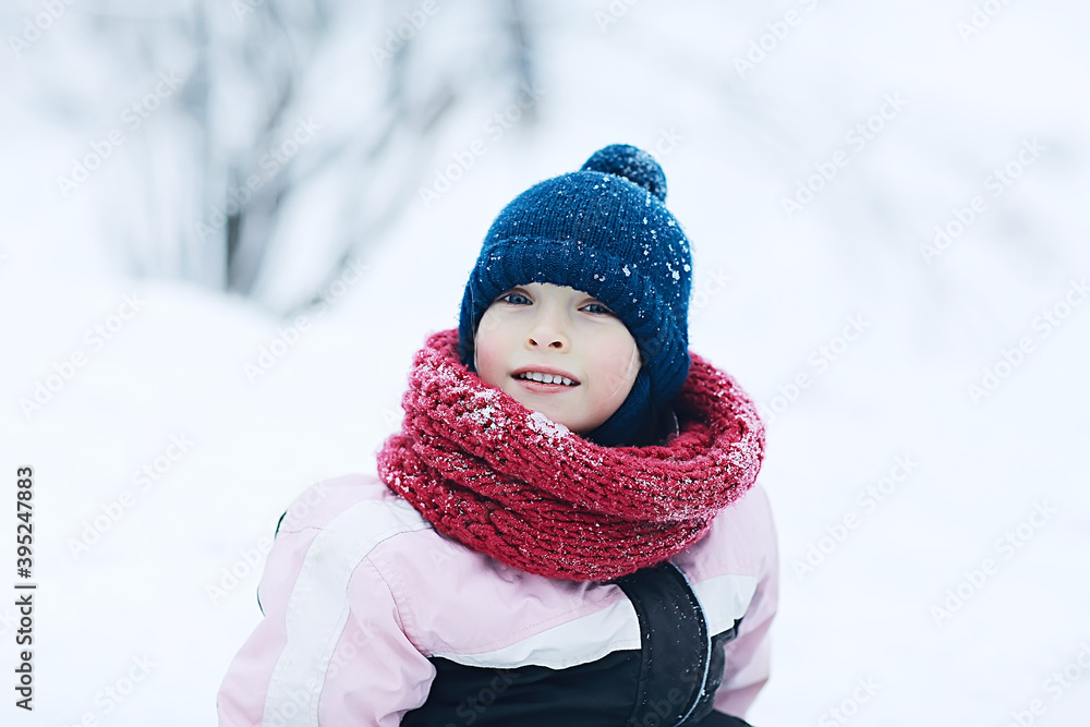 child  playing in the snow / the girl in warm sports clothes is playing with snow on a winter walk. Warm woolen hat, down jacket. Concept of a happy baby walk.