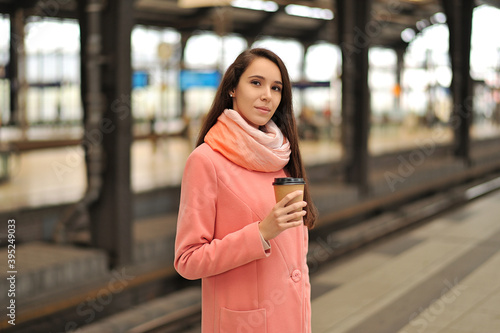 A girl at the station with a plastic cup of coffee