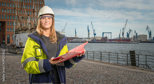 female engineer holding a clipboard in front of hamburg port background