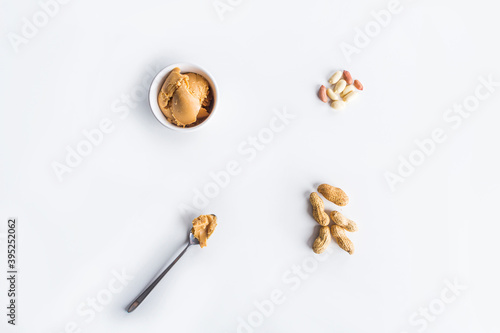 Pattern from Homemade Creamy peanut butter or paste in spoon and raw unpeeled groundnut on white background. Delicious breakfast or snack concept