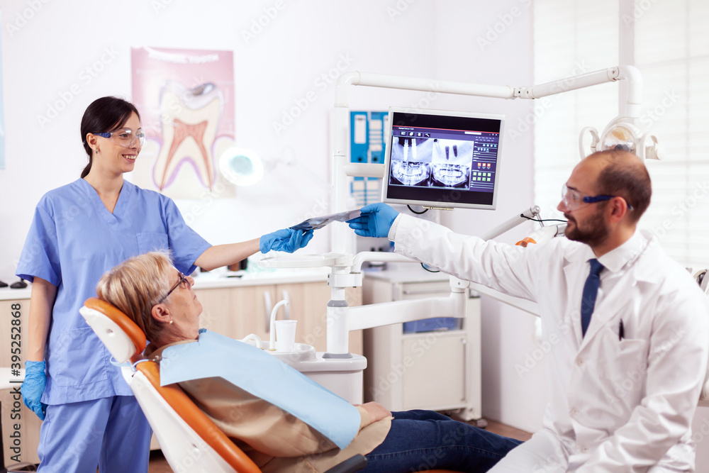 Dentist assistant giving doctor radiography of senior woman waiting. Medical teeth care taker holding patient radiography sitting on chair during consultation. Dentist assistant giving doctor radiography of senior woman waiting. Medical teeth care taker holding patient radiography sitting on chair during consultation.