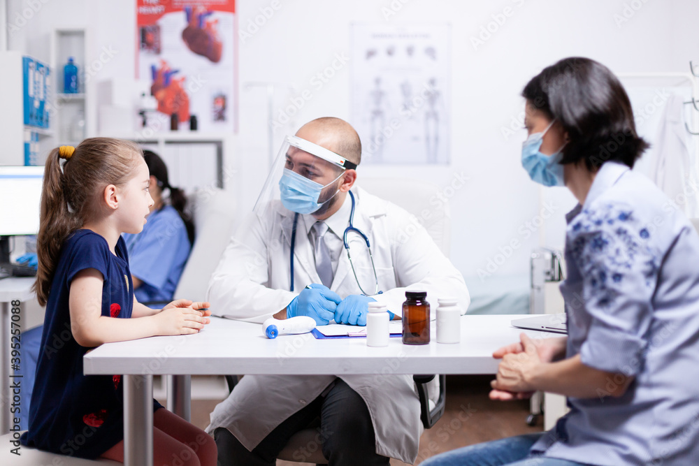 Child talking with pediatrician during consultation in hospital office. Health doctor specialist providing health care services consultations treatment in protective equipment.