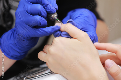 Close Up shot of hardware manicure in a beauty salon. Manicurist in protective gloves is applying electric nail file drill to manicure on female fingers.