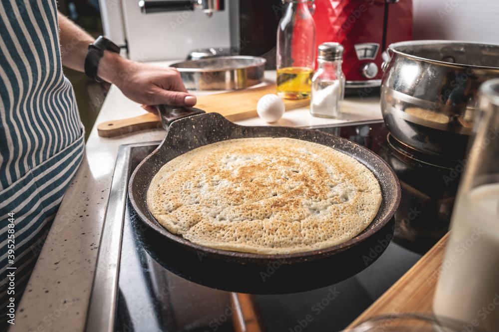 Woman is standing at the stove and frying pancakes in a pan. Concept of the process of making a tasty breakfast at home Woman is standing at the stove and frying pancakes in a pan. Concept of the process of making a tasty breakfast at home