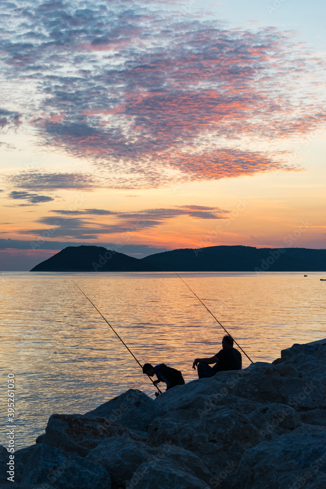 two men fishing on the seashore at sunset two men fishing on the seashore at sunset