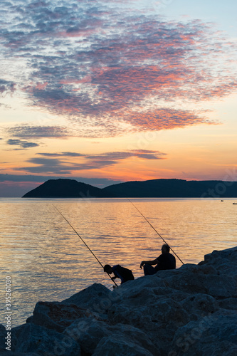 two men fishing on the seashore at sunset