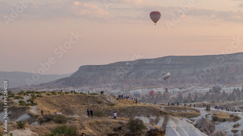 People watching a beautiful sunrise with colorful hot air balloons flying in clear morning sky aerial timelapse in Cappadocia, Turkey