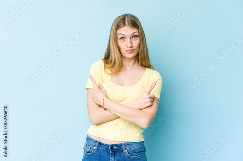 Young blonde woman isolated on blue background points sideways, is trying to choose between two options.