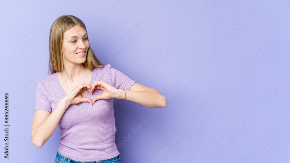 Young blonde woman isolated on purple background smiling and showing a heart shape with hands. Young blonde woman isolated on purple background smiling and showing a heart shape with hands.