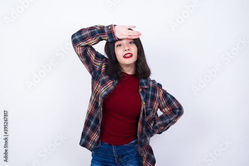 Young Caucasian beautiful woman wearing plaid shirt against white wall wiping forehead with hand making phew gesture, expressing relief feels happy that he prevented huge disaster. It was close enough photo