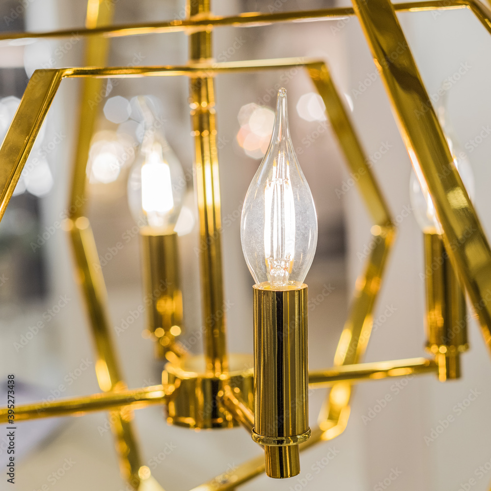 Luminous ceiling chandelier made of yellow gold metal with transparent glass lamps in the form of candles. Concept of interior decoration. Indooors. Close up.