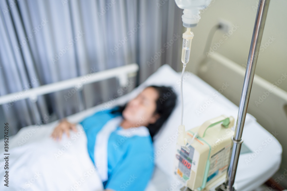 Focus on a saline dropper to female patient sleeping on the patient bed in the room after surgery at the hospital. Focus on a saline dropper to female patient sleeping on the patient bed in the room after surgery at the hospital.