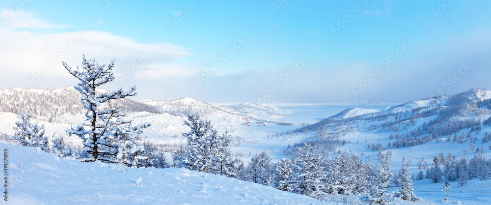 Beautiful landscape of frozen Lake Baikal on a sunny winter day. Panoramic views of the snow-covered Kurkut Bay and tourist wooden houses on the shore from the hill. Winter vacation