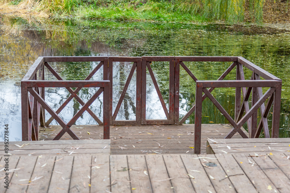 A small wooden pier for boats at the abandoned city pond with duckweed