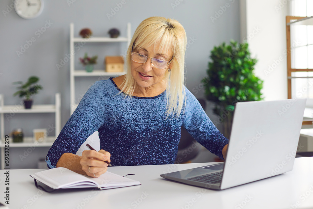 Senior female manager works with a laptop and writes down the information she has just read. Senior female manager works with a laptop and writes down the information she has just read.