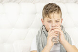 Sick boy sitting on a bed and drink water from a glass.