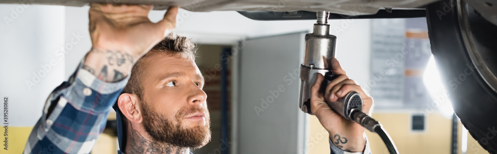 Obraz premium repairman fixing car detail with pneumatic wrench, 