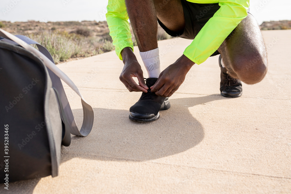 Close-up of the hands of a young black runner with a bag and a yellow rain jacket who ties his laces and prepares to train. Close-up of the hands of a young black runner with a bag and a yellow rain jacket who ties his laces and prepares to train.