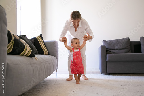Принти на полотні Front view of mom holding little girl hands and helping to walk