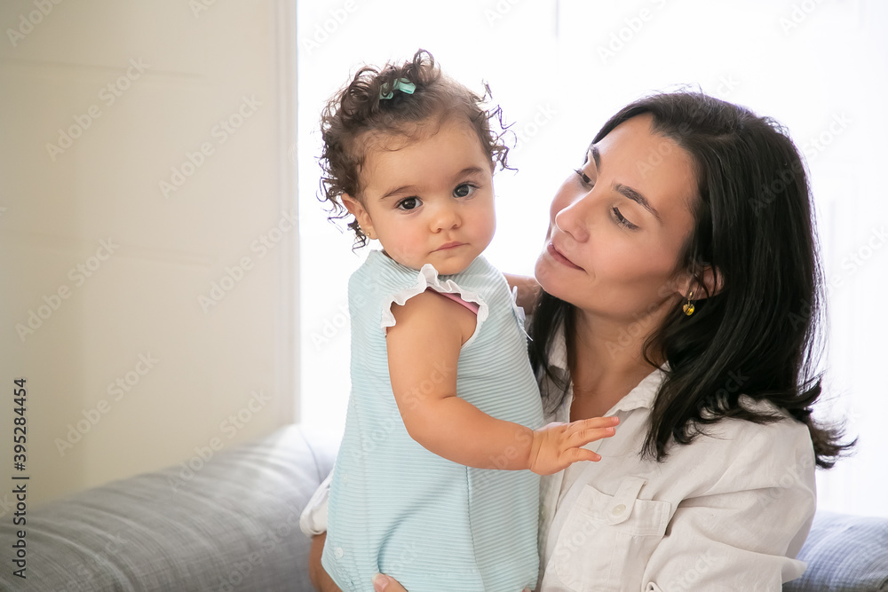 Cheerful mom holding sweet baby daughter in arms. Cute little girl looking at camera. Copy space. Parenthood and childhood concept Cheerful mom holding sweet baby daughter in arms. Cute little girl looking at camera. Copy space. Parenthood and childhood concept