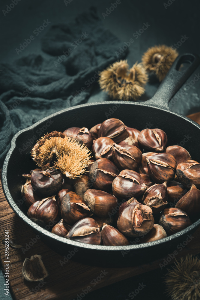 Cast iron pan with roasted chestnuts on a black background, vertical stock photo. Cast iron pan with roasted chestnuts on a black background, vertical stock photo.