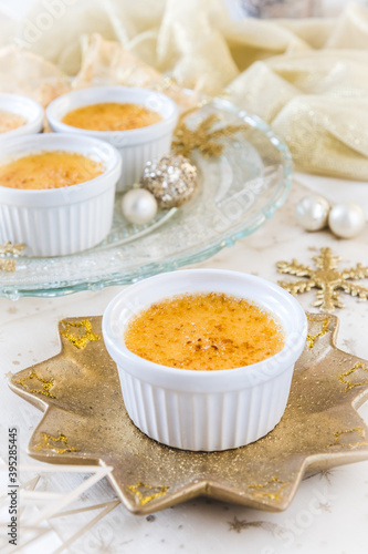 Creme brulee - traditional french vanilla cream dessert with caramelised sugar on top, served on a gold star-shaped plate with gold and white christmas decoration. Vertical stock photo.