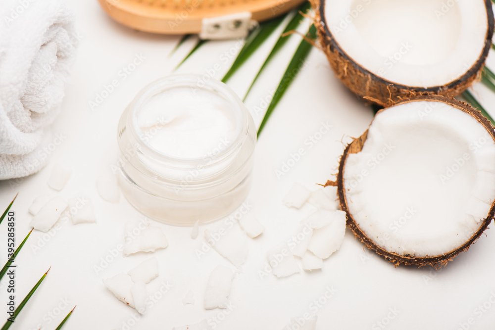 Coconut halves, flakes, container with cosmetic cream and towel on white Coconut halves, flakes, container with cosmetic cream and towel on white