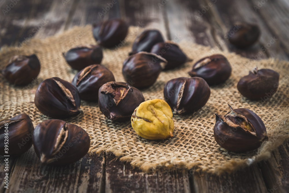 Roasted chestnuts, one peeled, on a dark wooden background
